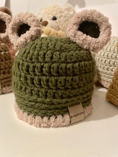 Crocheted green and pink hat with ears, resembling a cute animal design.